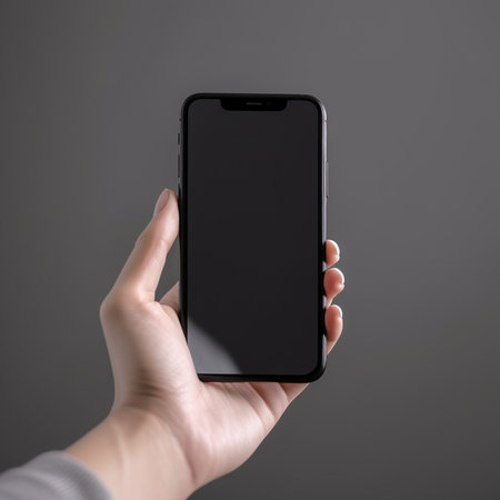 female hand holding a black smartphone with blank screen isolated on gray backgroundの素材