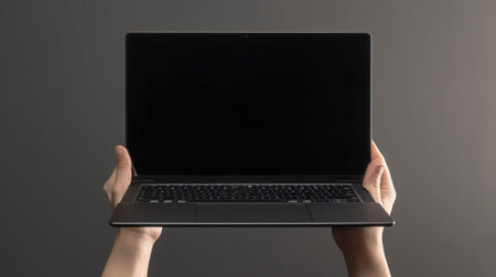 Female hands holding a laptop with blank screen on gray background, close upの素材