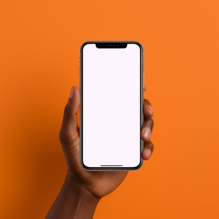 African american man holding smartphone with blank screen on orange background, mockupの素材