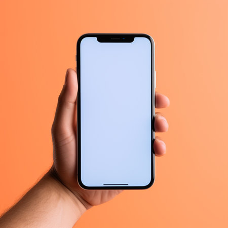 Male hand holding smartphone with blank screen on orange background, closeupの素材