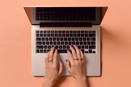 Top view of female hands typing on laptop keyboard on a pink backgroundの素材