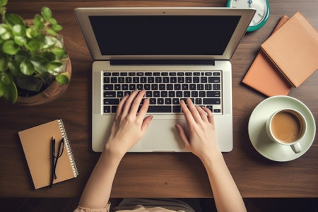 Top view of female hands typing on laptop keyboard with cup of coffee on tableの素材