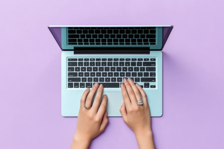 Top view of female hands typing on laptop keyboard on purple background.の素材