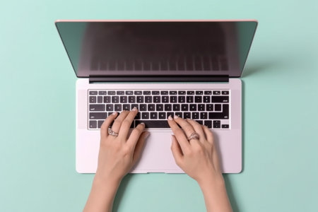 Top view of female hands typing on laptop keyboard on pastel blue backgroundの素材
