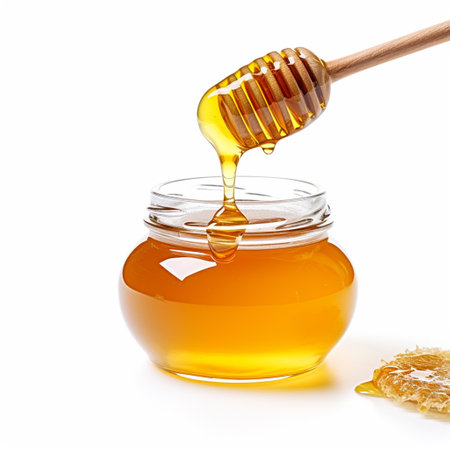 Honey dripping from a wooden honey dipper into a jar isolated on white backgroundの素材