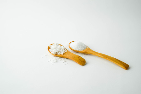 salt and sugar on small wooden spoon on white backgroundの写真素材