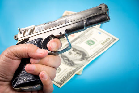 hand holding a gun and money background on blueの写真素材