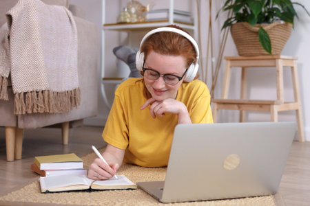 young Caucasian woman with red hair resting at the computer, listening to music, stretching,...