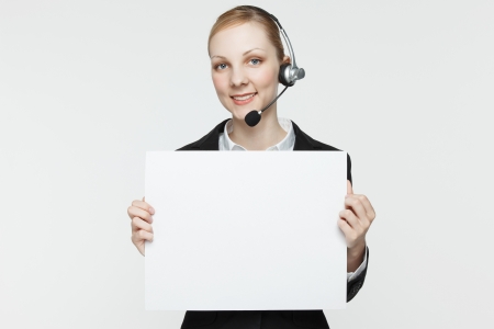 Pretty, smiling woman wearing a headset and holding a blank sign.の写真素材