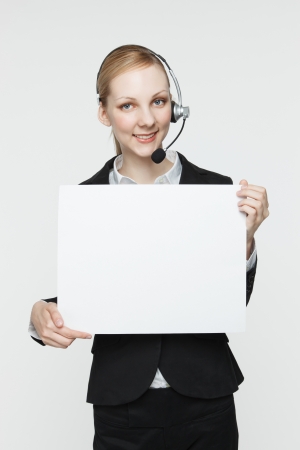 Pretty, smiling woman wearing a headset and holding a blank sign.の写真素材
