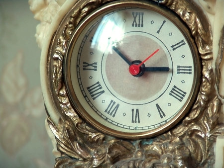 Old antique gilded clock with Roman numerals on a background of olive wallpaper