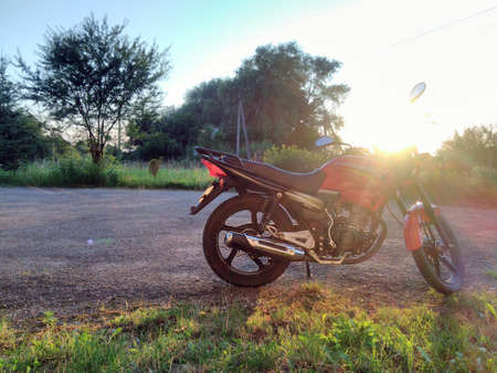 Red motorcycle in the countryside on a background of trees and sunset in summerの写真素材