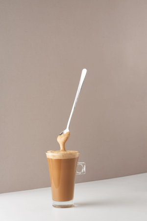 Glass cup with cappuccino and fragrant foam and spoon. Cup with cappuccino, latte or coffee with milk. Creative design for cafes and restaurants with a cup of coffee.の写真素材