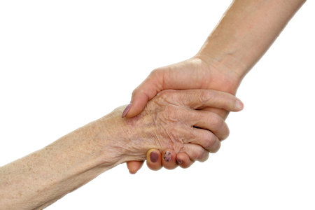 Hands of young adult and senior women. Senior and young holding hands outside. Elderly concept with light backgroundの写真素材