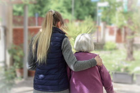 Young carer walking with the elderly woman in the garden with light backgroundの写真素材