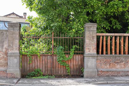 Gate of abandoned old house. Old rusty gate. Sidewalk near old house with garden overgrown with bushes.の写真素材