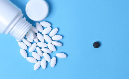 White pills and a black pill. Different pills. Medical and different concept of light blue paper...