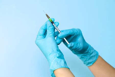 Hands in blue gloves holding a plastic syringe with liquid for injection on light blue background. Health care, treatment concep.の写真素材