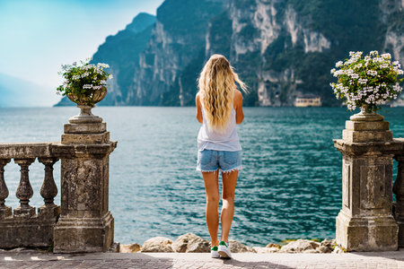 Young girl looks on the mountain and blue water of the Garda lake. Back view, vacation conceptの写真素材