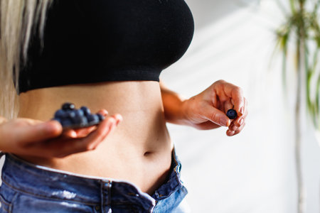 <p>First month of pregnancy. Young girl with sporty physique holds blueberries in hand. Motherhood and healthy concept</p>の写真素材