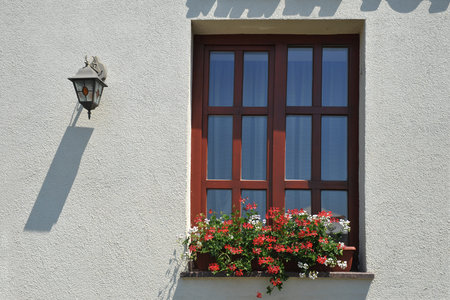 Facade of the house with flowers on the windowsill and a lantern on the wall