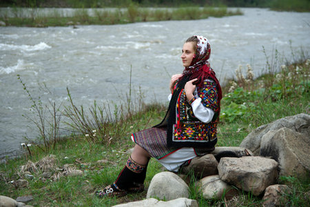 Ukrainian hutsul woman in authentic national costume sitting on a stone on the bank of the Cheremosh...