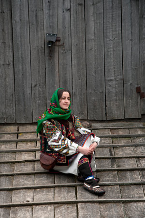 A girl in an authentic national hutsul costume sits on the floor near the barn door