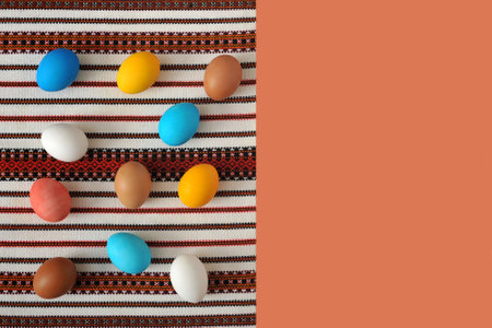 Multicolored Easter eggs lie on an embroidered tablecloth. Space for text on pink background.の写真素材