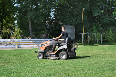 Driver on mower cutting grass lawn in football field