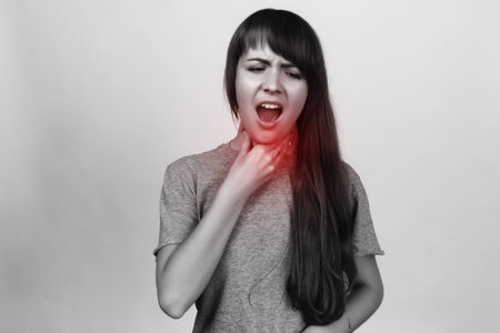Sore throat. Young woman hand touching her Ill neck over gray backgroundの写真素材