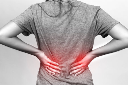 Pretty woman suffers from backache standing black and white with red accent over gray background