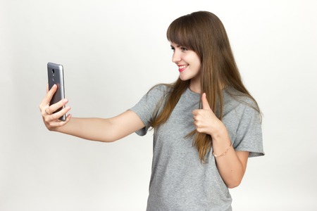 Portrait of a pretty woman she smiles and makes selfie  standing over gray backgroundの写真素材