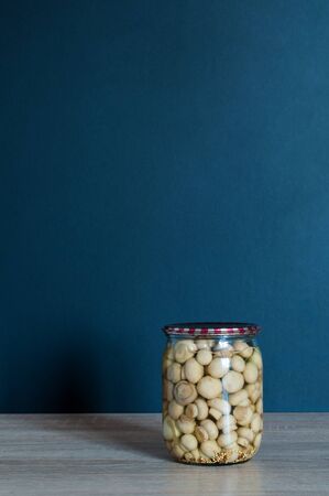 Pickled champignon mushrooms in jar on the wooden table in front of black wallの写真素材
