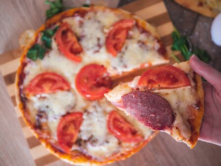 Hand picking slice of homemade pepperoni pizza. Pizza party. Hot italian pepperoni pizza on wooden background.の写真素材