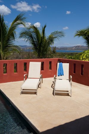 two lounge chairs on a pool deck with Playa Flamingo Costa Rica in the background