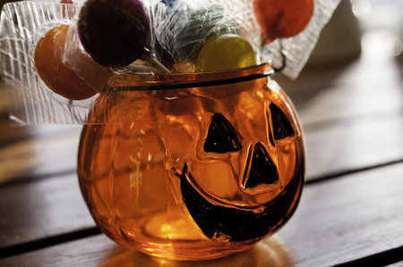 Glass jack-o-lantern filled with lollipops sitting on a wooden tableの写真素材