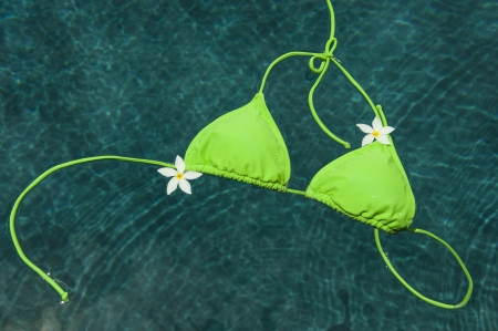 Green bikini top floating in pool with Pulmeria flowersの写真素材
