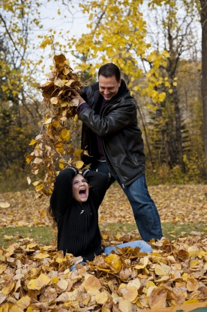 Father dropping a handful of leaves on his daughter while playingの写真素材