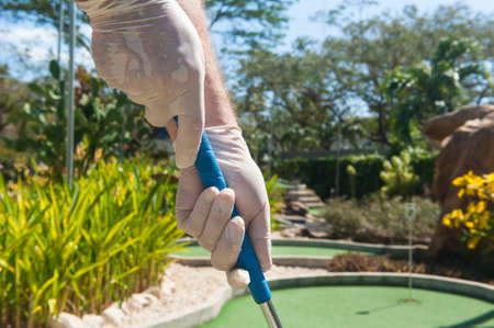 Gloved hands holding a blue mini golf club in the sunの写真素材