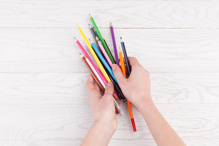 Colour pencils in hands on white wooden backgroundの写真素材