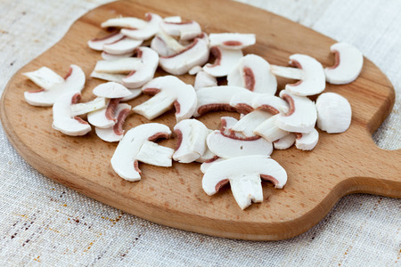 Sliced fresh white button mushrooms on a wooden chopping boardの写真素材
