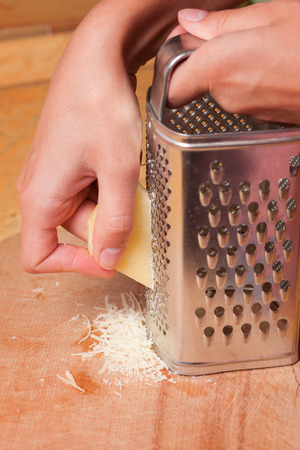 cooking, food and home concept - close up of female hands grating cheeseの写真素材