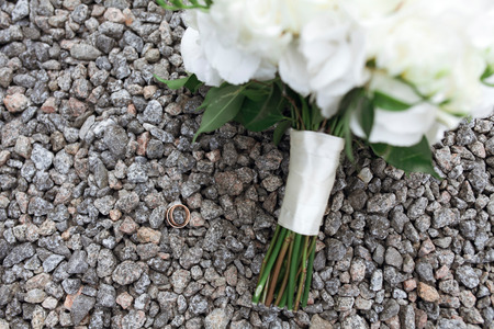 Brides rustic bouquet of white roses and golden rings on stones rock backgroundの写真素材
