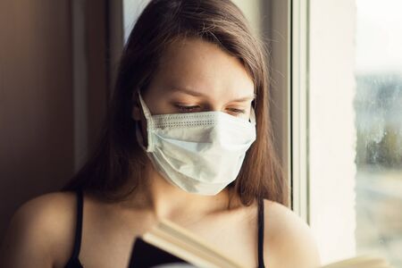 Portrait of young girl with ear loop face mask reading the bookの写真素材