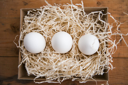 Three white eggs in nest, wooden background