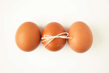 Three brown eggs wrapped with thread on white background.の写真素材