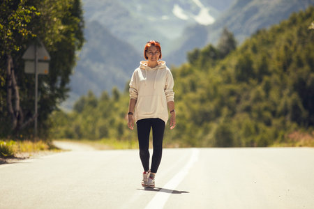 Young woman walking on the road. Mountain landscape, summer.