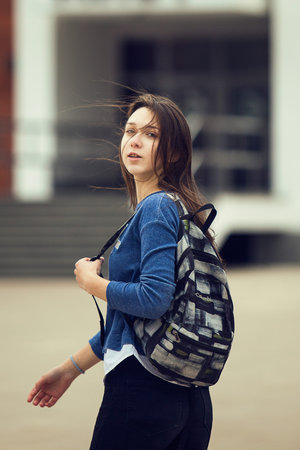 Young girl with college bag, wind blow her hair about. student with bagpack. Autumn, street.