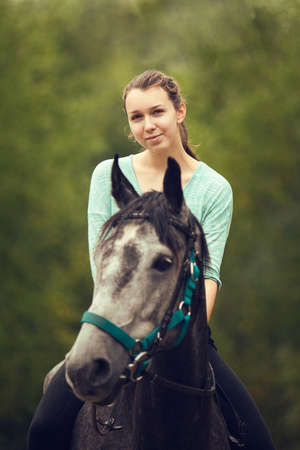Young girl sits astride a gray horseの写真素材
