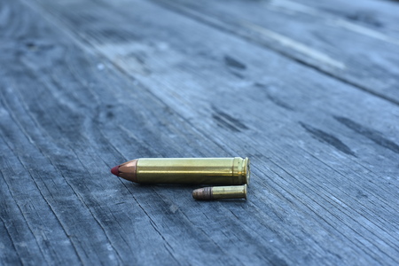 Red tip 450 Caliber ammunition and 22 Caliber side way on wooden backgroundの写真素材